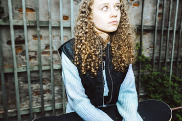 Contemplative girl with curly hair looking away against wall - MASF42128