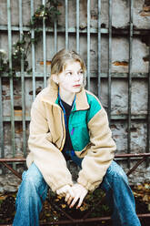 Contemplative girl wearing warm clothing while sitting on railing against wall - MASF42129