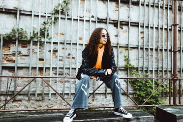 Teenage girl with sunglasses sitting on railing against wall - MASF42130