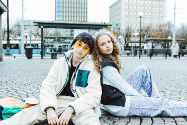 Portrait of male and female friends sitting on footpath in city - MASF42138