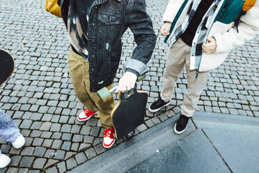 Low section of boy with skateboard standing by male friend on footpath - MASF42145
