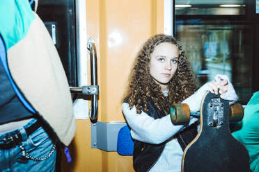 Portrait of confident girl with skateboard sitting in tram while traveling during weekend - MASF42163