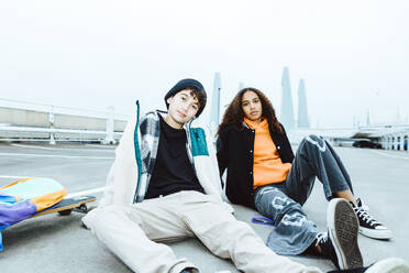 Portrait of male and female friends sitting on street against clear sky - MASF42182