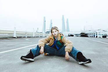 Portrait of confident girl sitting on street against clear sky - MASF42186