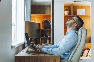 Thoughtful freelancer sitting with laptop at home office - OLRF00070