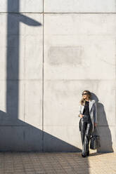 Businesswoman with hand in pocket leaning on wall - DLTSF03743