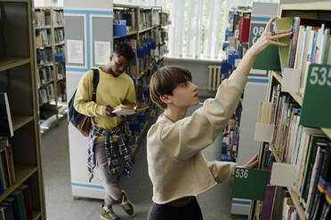 Studentin nimmt Buch aus oberstem Regal in der Bibliothek - DSHF01495