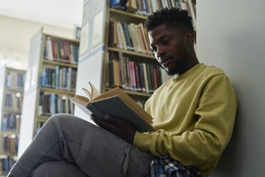 Student leaning on shelf and reading book in library - DSHF01501