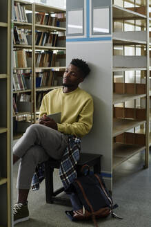 Müder Student mit geschlossenen Augen in der Bibliothek - DSHF01502