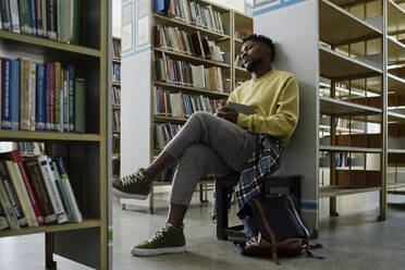 Studentin ruht sich in der Nähe von Bücherregalen in der Bibliothek aus - DSHF01503