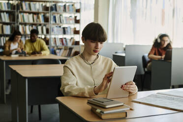 Young student using tablet PC at desk in library - DSHF01505