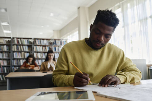 Junge Studentin schreibt in ein Buch am Schreibtisch - DSHF01513