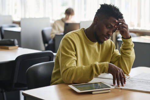 Müder Student studiert am Schreibtisch in der Bibliothek - DSHF01515