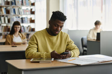 Junge Studentin benutzt ihr Smartphone in der Bibliothek der Universität - DSHF01517