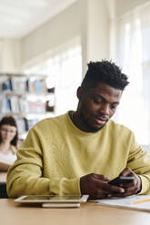 Junge Studentin benutzt Smartphone in der Bibliothek - DSHF01518