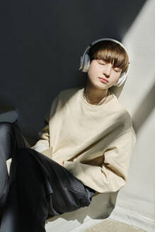 Junge Frau mit drahtlosen Kopfhörern, die an der Wand lehnt und Musik hört - DSHF01523
