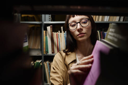 Junge Studentin auf der Suche nach Büchern im Regal in der Bibliothek - DSHF01526