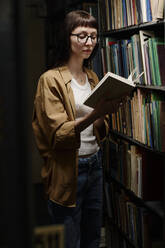 Ein Student liest ein Buch in der Nähe eines Regals in der Bibliothek - DSHF01528