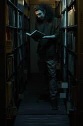 Ein Student liest ein Buch und steht inmitten von Regalen in einer Bibliothek - DSHF01538