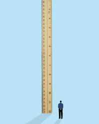 Man standing near oversized ruler against blue background - GWAF00446