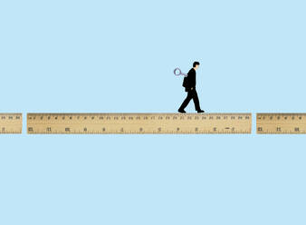 Man walking on broken ruler with wind-up key against blue background - GWAF00447