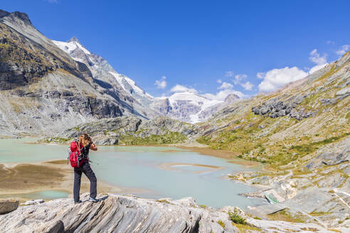 Frau steht auf einem Felsen und fotografiert den Gletscher Pasterze am Großglockner, Österreich - FOF13713