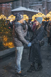 Smiling couple holding hands and standing in Christmas market - TILF00037