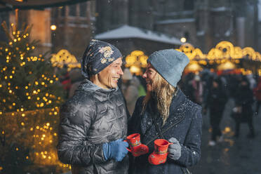 Happy couple holding cups of punch in Christmas market - TILF00038