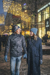 Happy couple holding hands and standing in Christmas market - TILF00045