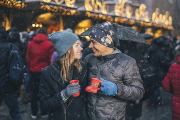 Smiling couple holding cups of punch drink in winter - TILF00047