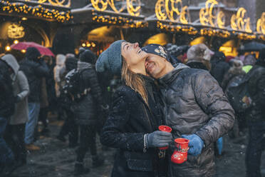 Glücklicher Mann umarmt Frau auf dem Weihnachtsmarkt - TILF00049