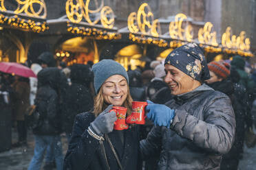 Happy man and woman toasting cups of punch drink in Christmas market - TILF00050