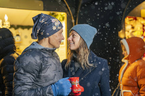 Loving couple holding cups of punch and enjoying in Christmas market - TILF00051