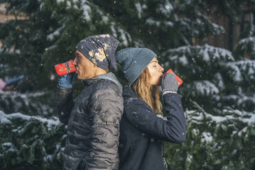 Man and woman drinking cups of punch near fir tree in winter - TILF00052