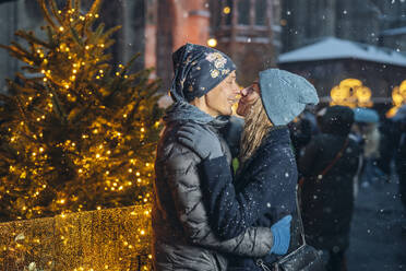 Loving couple embracing and rubbing noses near illuminated Christmas tree - TILF00056