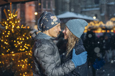 Glücklicher Mann und Frau stehen neben einem beleuchteten Weihnachtsbaum im Winter - TILF00057