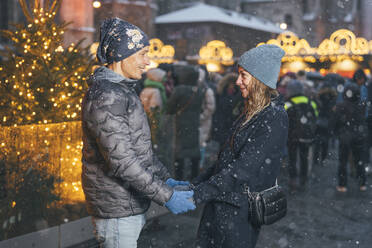 Happy couple holding hands and standing at Christmas market in winter - TILF00058