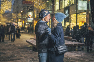 Happy loving couple dancing in snow at Christmas market - TILF00062