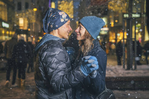 Lächelndes Paar tanzt im Schnee auf dem Weihnachtsmarkt - TILF00063