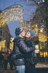 Man kissing woman on cheek at Christmas market - TILF00064