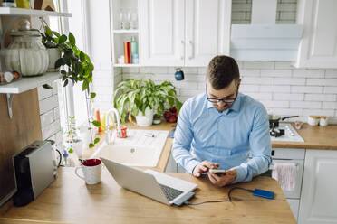 Freelancer using mobile phone at table in kitchen - OLRF00084