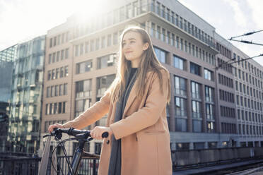 Smiling teenage girl with bicycle in city - TAMF04047