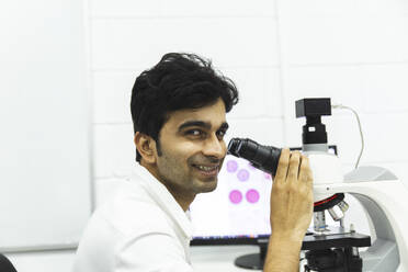 Smiling scientist holding microscope at laboratory - PCLF00882