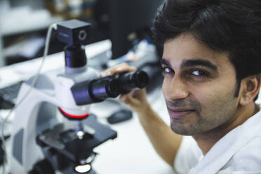 Smiling scientist near microscope at laboratory - PCLF00883