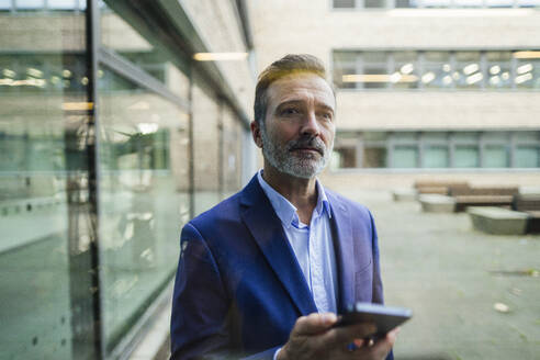 Nachdenklicher Geschäftsmann hält Smartphone durch Glas gesehen - JOSEF22437