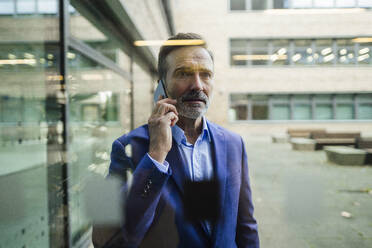 Businessman talking on smart phone seen through glass - JOSEF22440