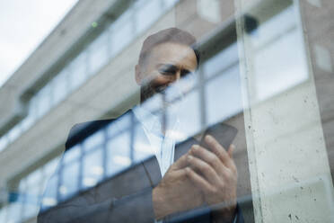 Businessman using mobile phone seen through glass - JOSEF22445