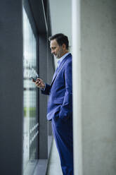 Geschäftsmann benutzt Smartphone in der Nähe eines Glasfensters im Büro - JOSEF22477