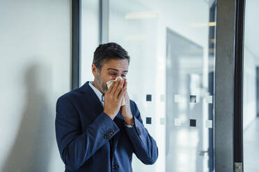 Businessman blowing nose on handkerchief in office - JOSEF22502