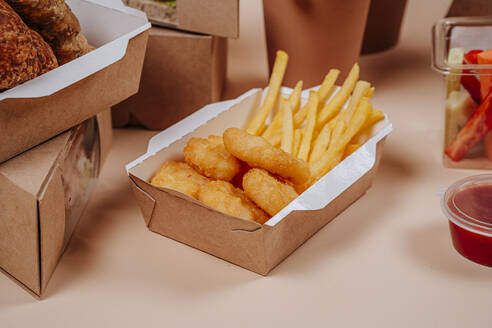 French fries and chicken nuggets in container against beige background - MDOF01778